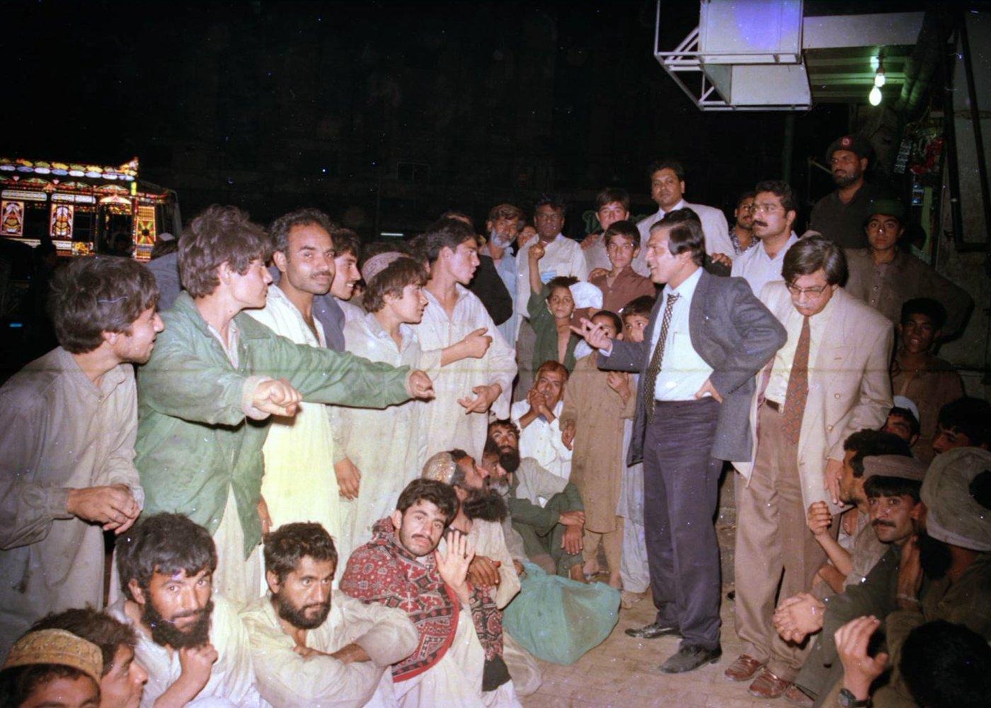 A team member addresses a gathering of men and boys at a night distribution point. A team member addresses a gathering of men and boys at a night distribution point.